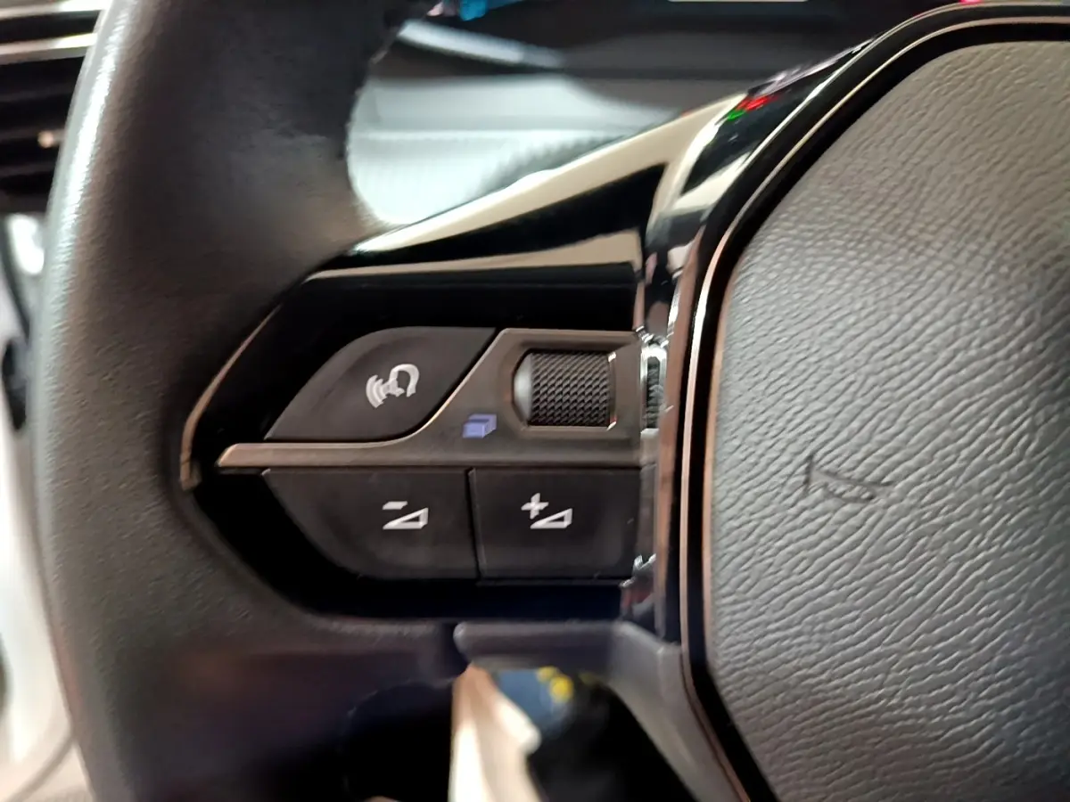 Gros plan sur les commandes gauche du volant noir d’une Peugeot 208 électrique blanche, boutons multifonctions visibles.