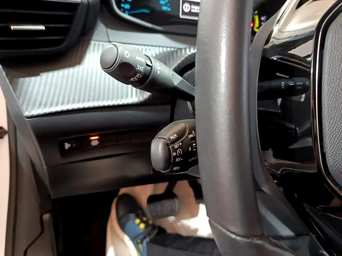 Gros plan sur le volant noir et les commandes de régulateur de vitesse de la Peugeot 208 électrique, tableau de bord partiellement visible.