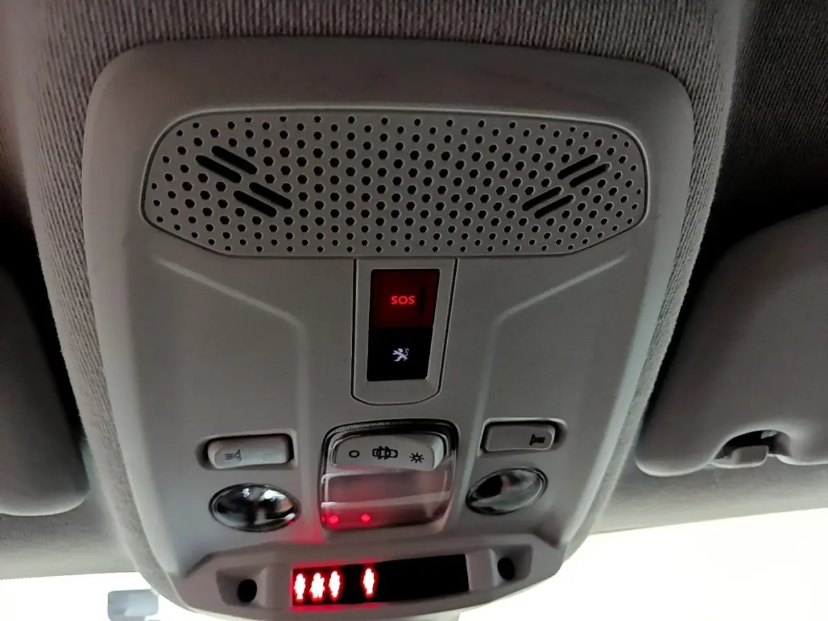 Vue en gros plan du plafonnier gris clair avec bouton SOS rouge et éclairage intérieur de la Peugeot 208 électrique blanche.