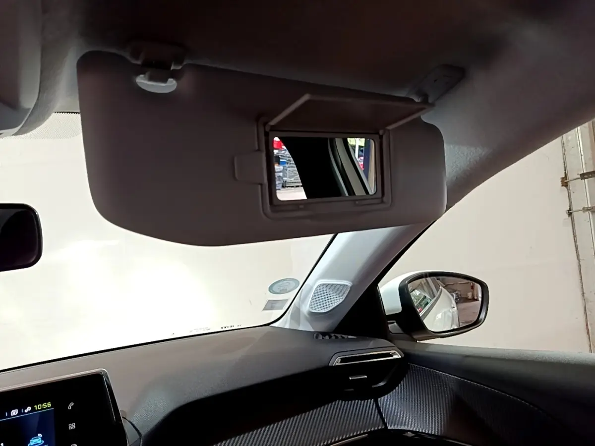 Intérieur de la Peugeot 208 électrique blanche, vue côté passager avec pare-soleil et rétroviseur extérieur visible.