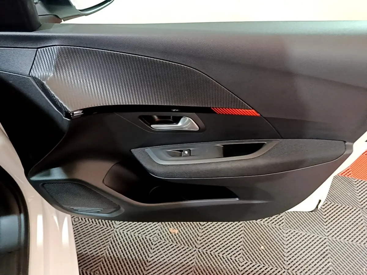 Vue rapprochée de la porte avant gauche noire avec insert décoratif gris et bande rouge d’une Peugeot 208 électrique blanche.