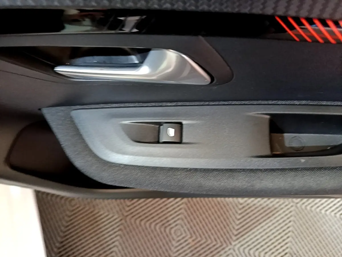 Gros plan sur la poignée intérieure et le bouton de lève-vitre côté conducteur de la Peugeot 208 électrique blanche.