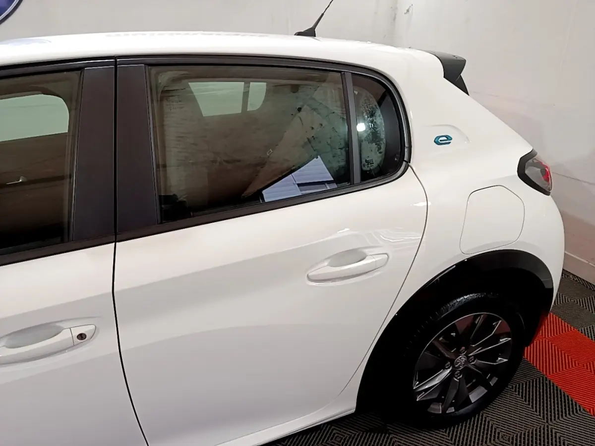 Vue latérale côté droit de la Peugeot 208 électrique blanche, mettant en valeur la porte arrière et le logo "e" bleu près de l'aile arrière.