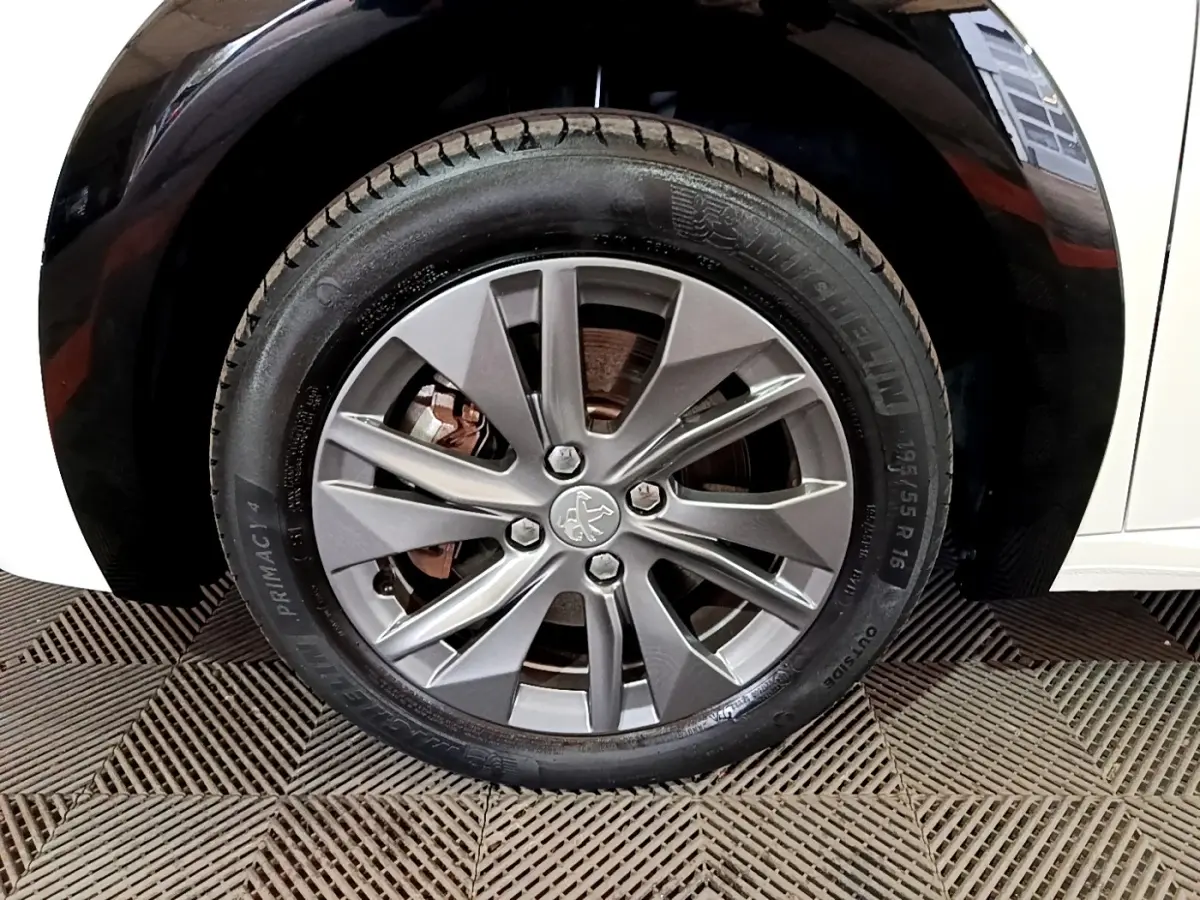 Gros plan sur la roue avant droite avec jante alliage grise de la Peugeot 208 électrique blanche.
