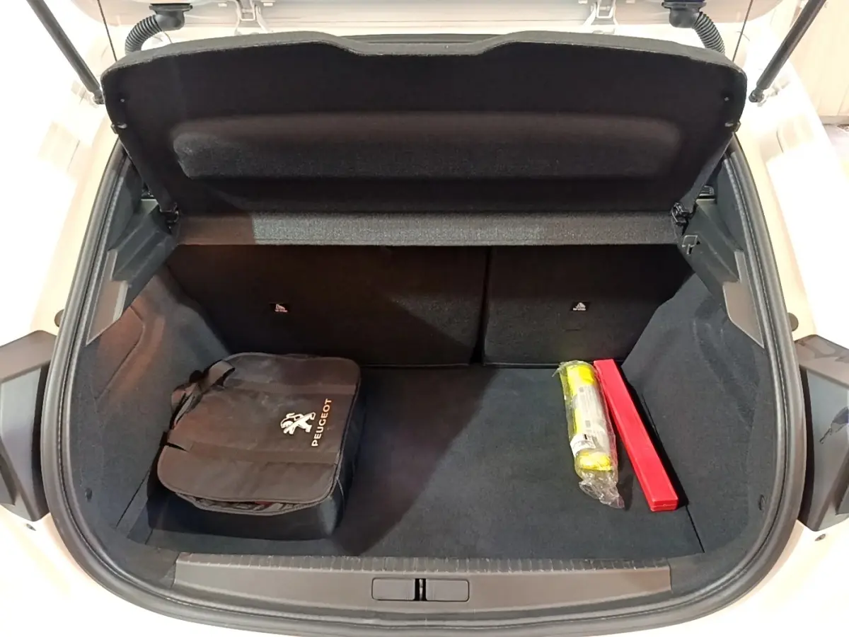 Coffre ouvert vu de l'arrière d'une Peugeot 208 électrique blanche avec trousse de secours et triangle de signalisation.