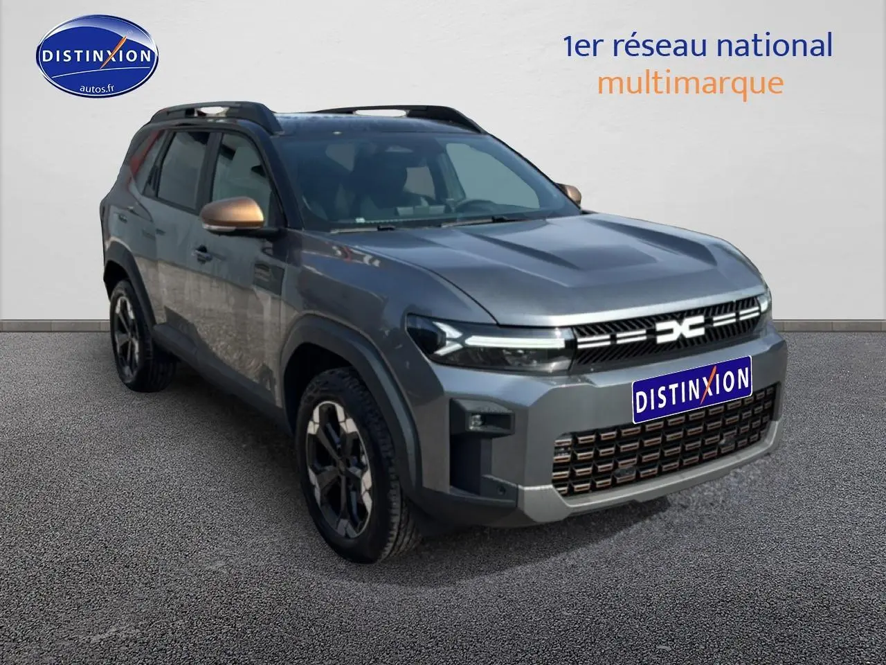 SUV Dacia Bigster gris schiste en 3/4 avant gauche avec jantes alu et barres de toit noires.