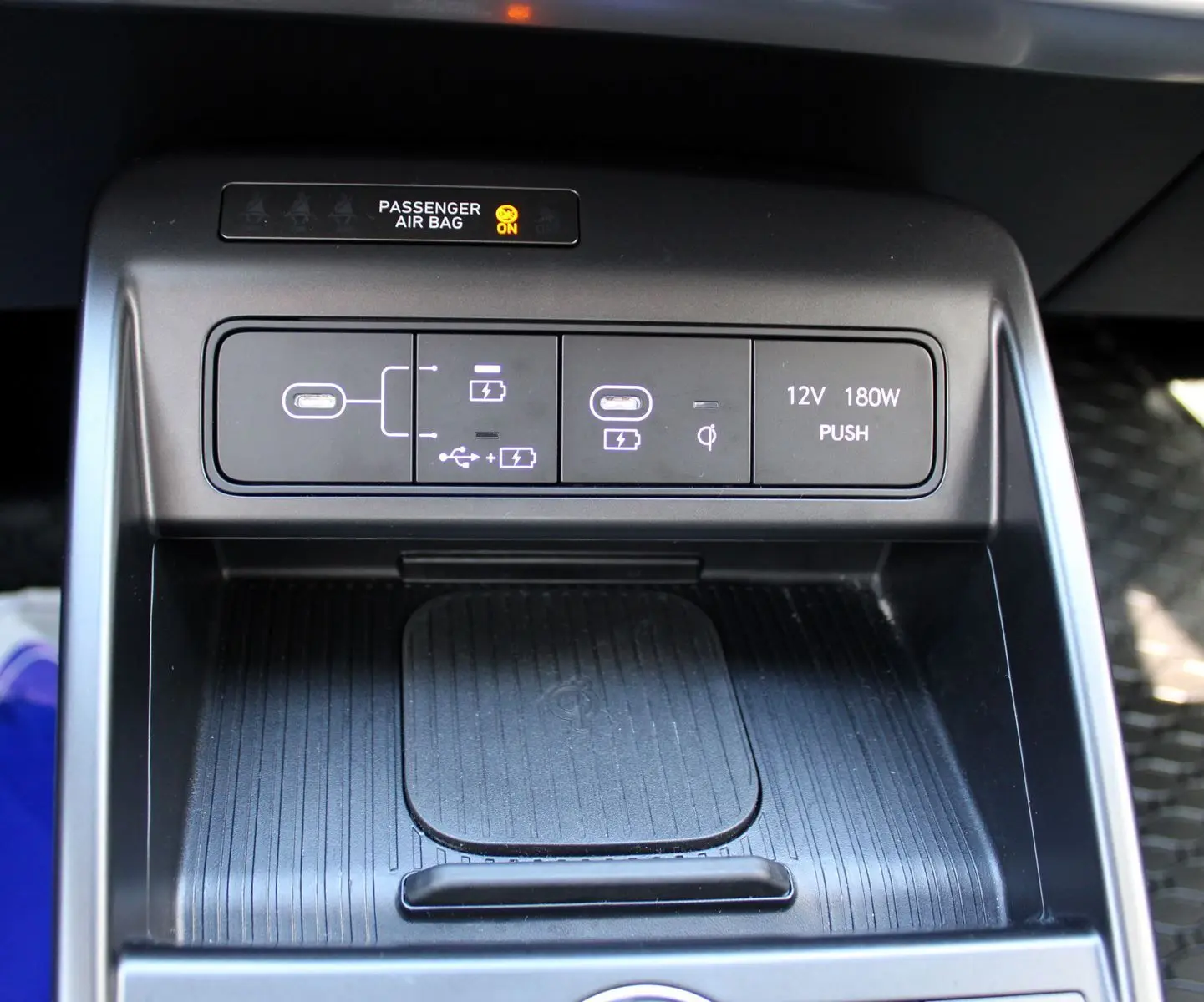 Gros plan sur la console centrale noire du Hyundai Kona 2024, montrant les ports USB, prise 12V et zone de recharge sans fil.