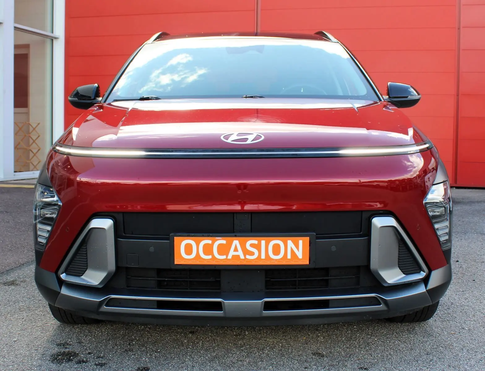 Vue avant d’un Hyundai Kona 2024 rouge Ultimate Metal avec détails noirs et plaque orange « Occasion » visible.
