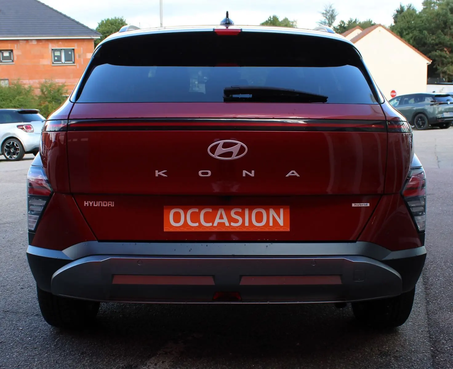 Vue arrière d'un Hyundai Kona 2024 rouge Ultimate Metal avec toit noir, badge hybride et plaque occasion.