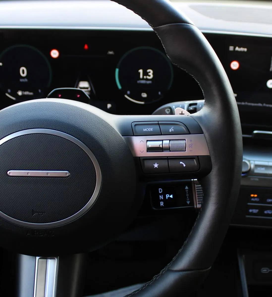 Gros plan sur le volant noir cuir du Hyundai Kona 2024, avec commandes intégrées et tableau de bord numérique en arrière-plan.