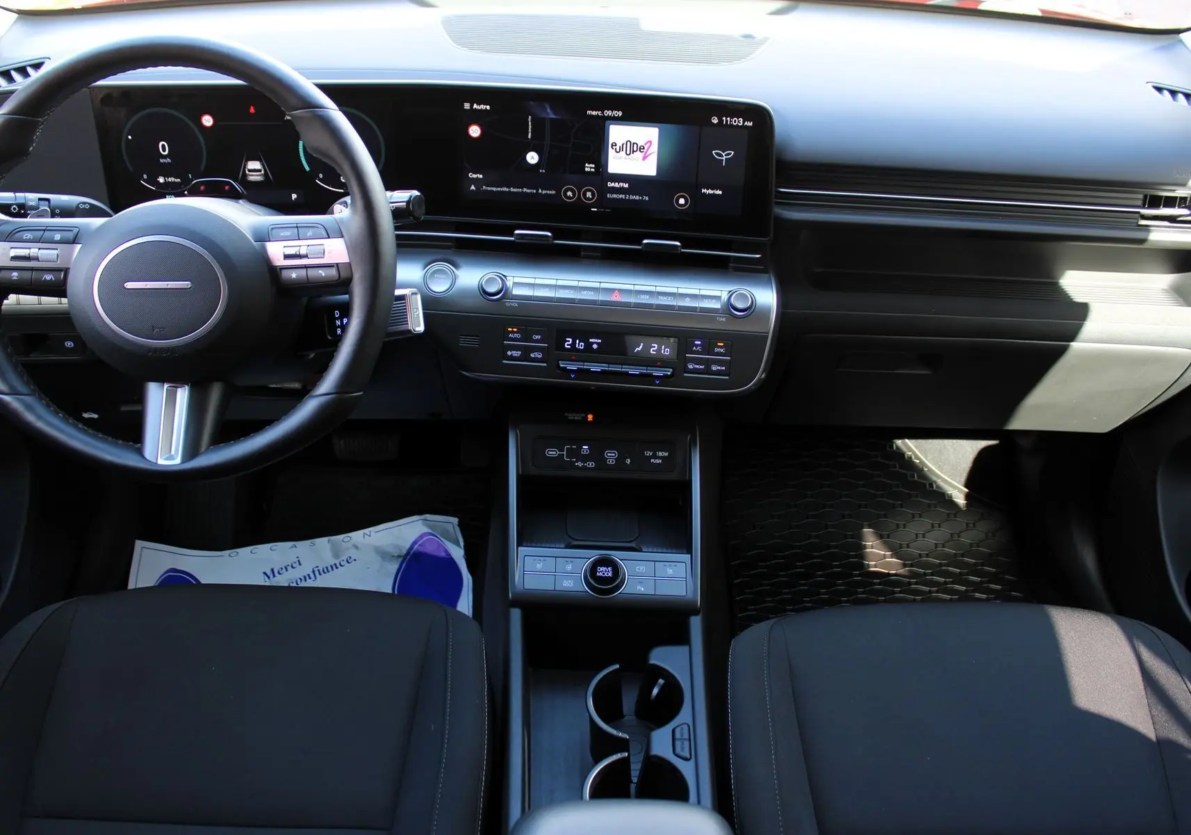 Vue intérieure avant du tableau de bord et console centrale noire du Hyundai Kona 2024 hybride avec écran tactile large et volant multifonction.