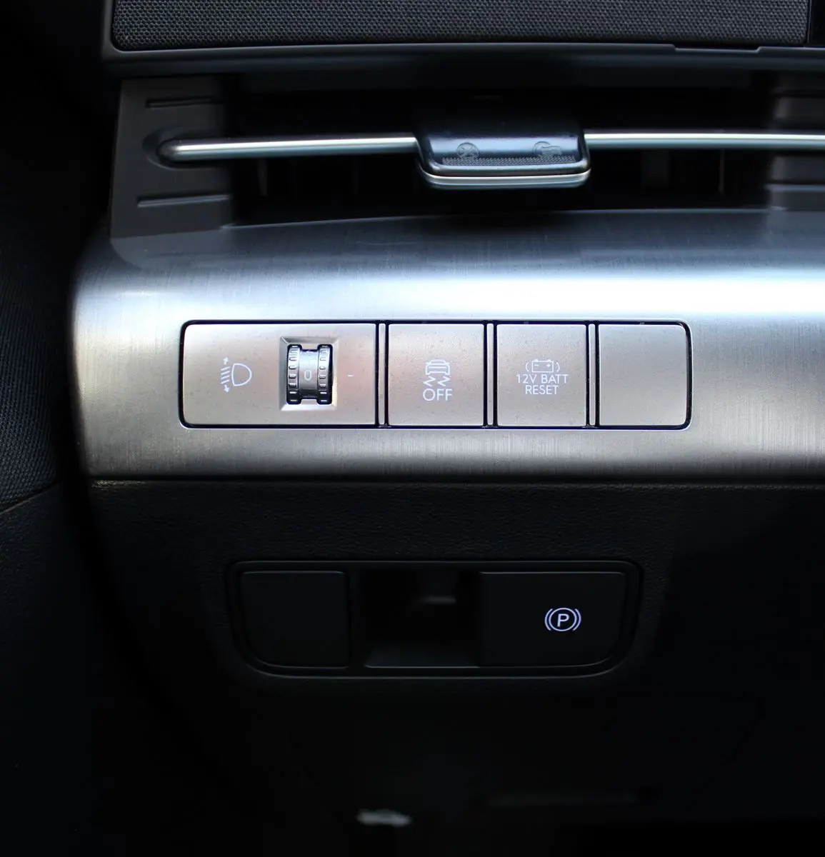 Gros plan sur les commandes argentées du tableau de bord du Hyundai Kona 2024, avec bouton frein à main électronique éclairé.
