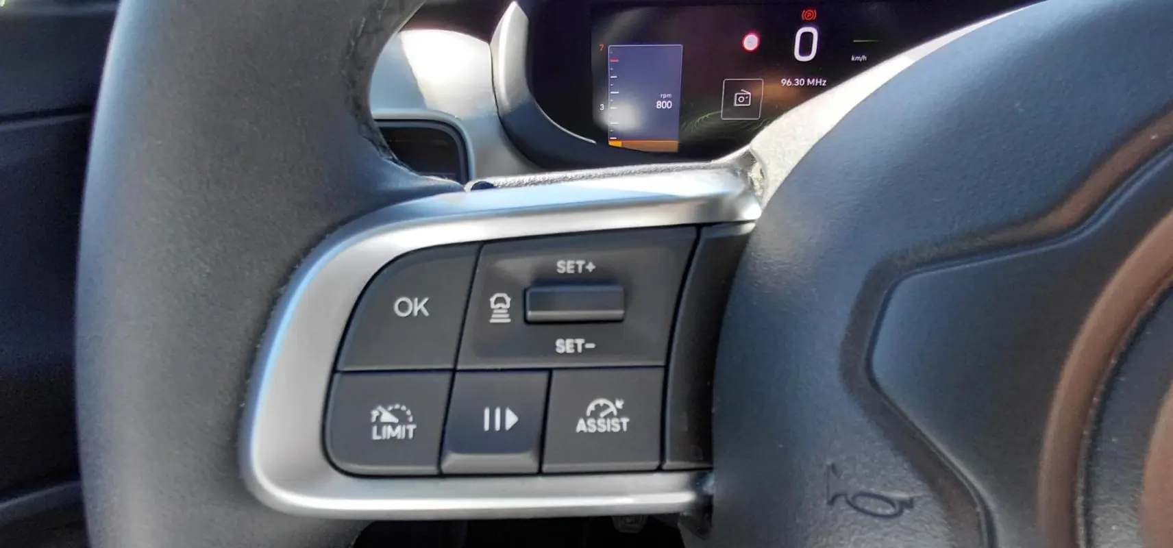 Gros plan sur les commandes à gauche du volant du Jeep Avenger blanc 2025, avec affichage numérique en arrière-plan.