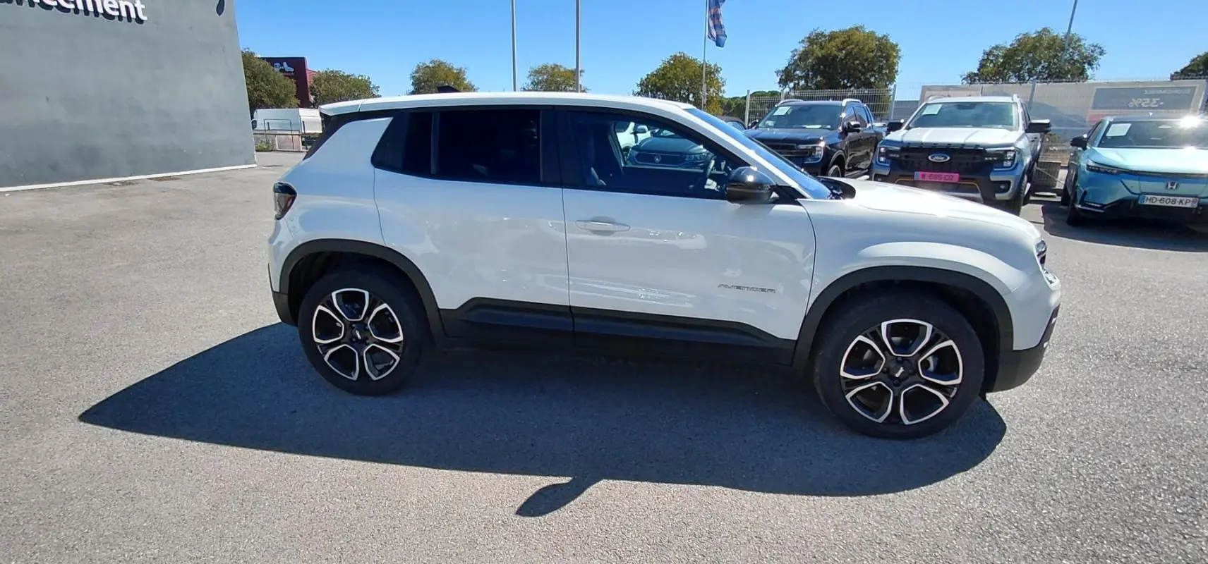 Vue de profil côté gauche d'un Jeep Avenger blanc 2025 avec jantes noires et détails noirs sur les bas de caisse.