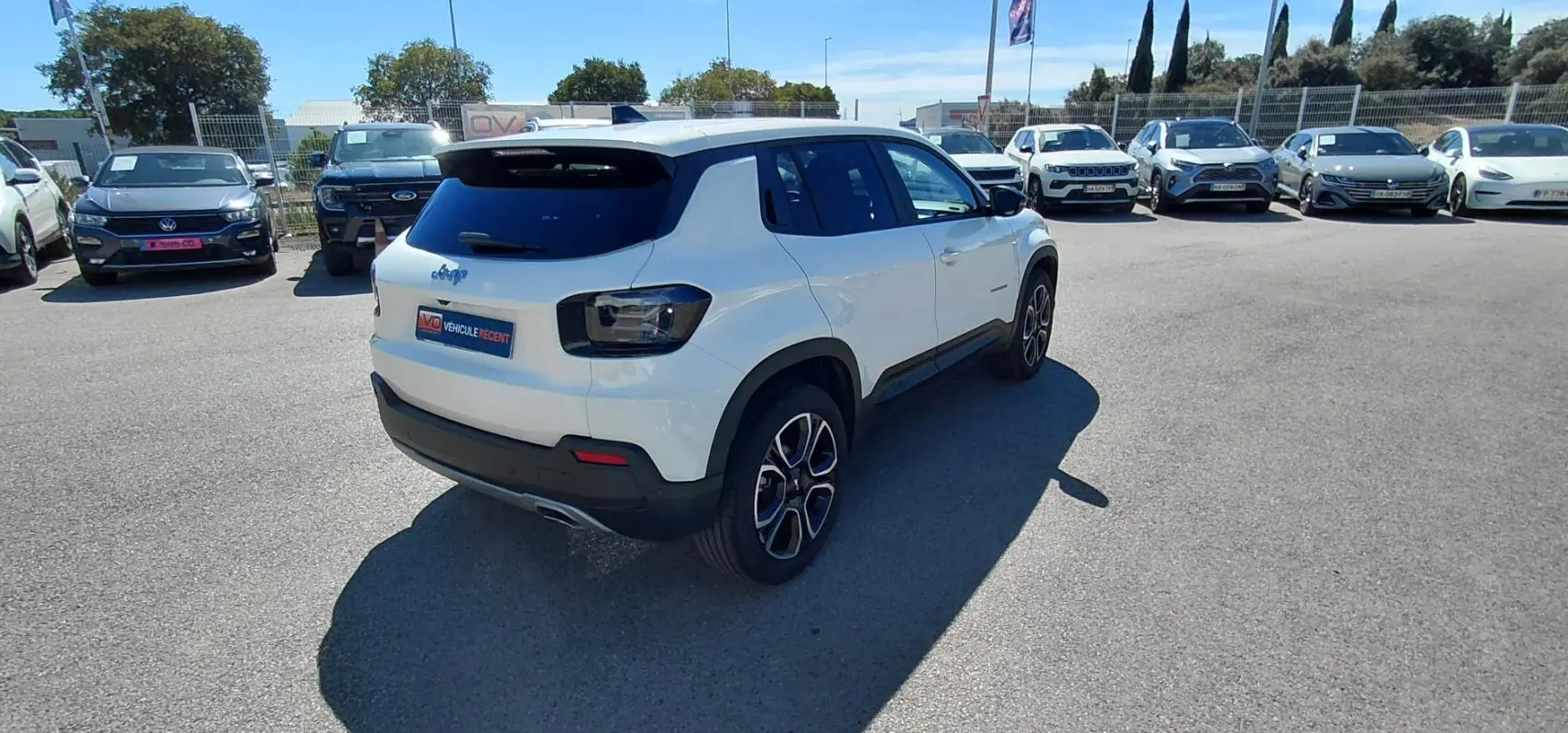 Jeep Avenger blanc en 3/4 arrière droit, avec feux arrière sombres et jantes alliage distinctives, sur parking extérieur.