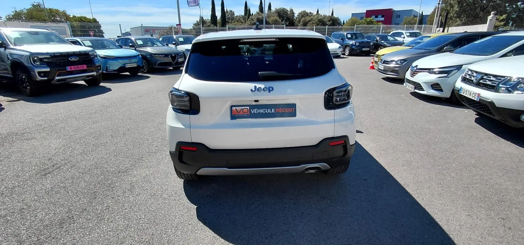 Vue arrière d'un Jeep Avenger blanc 2025 avec feux arrière noirs et pare-chocs noir contrastant sur parking.