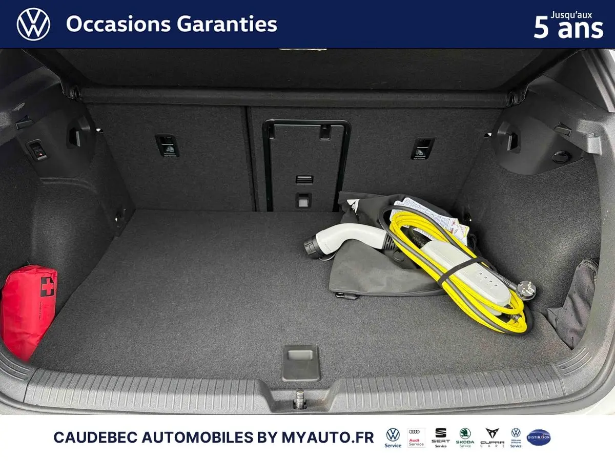Coffre ouvert d’une Volkswagen Golf blanche avec câble de recharge électrique et trousse de secours rouge visible.