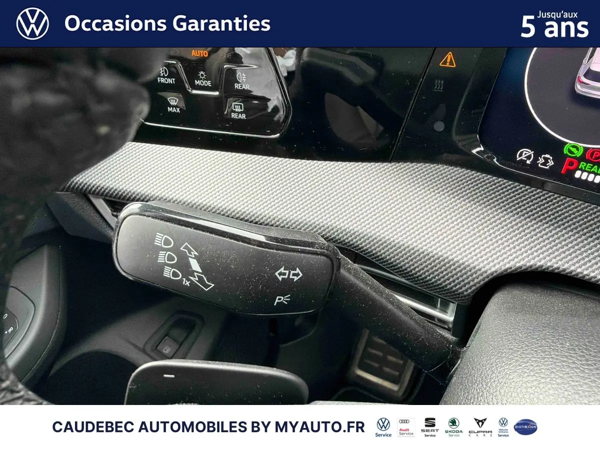 Gros plan sur la commande de clignotants et feux, tableau de bord noir avec finition carbone, intérieur Volkswagen Golf blanc.