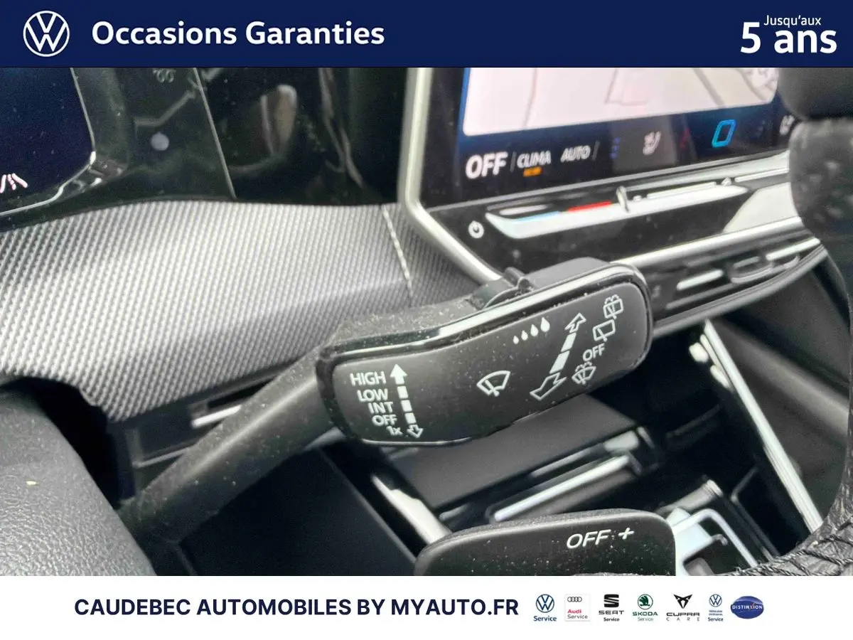 Gros plan sur la commande des essuie-glaces dans l'habitacle d'une Volkswagen Golf blanche, avec écran tactile en arrière-plan.