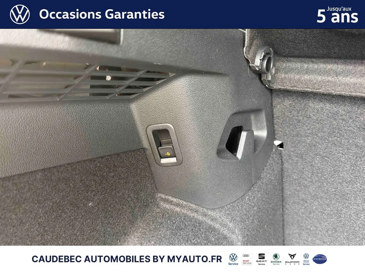Détail intérieur du coffre d’une Volkswagen Golf blanche, montrant un levier de rabattement des sièges.