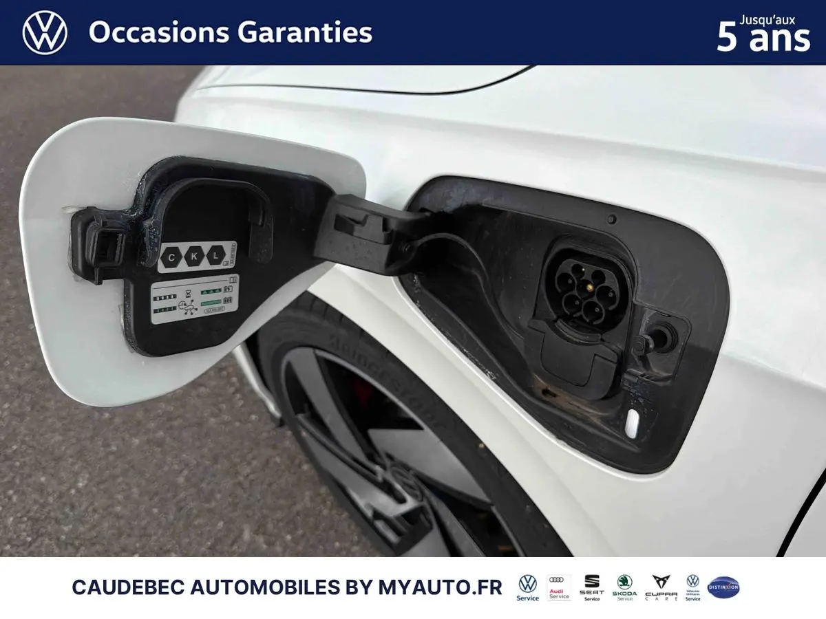 Prise de recharge ouverte côté arrière droit d’une Volkswagen Golf 1.5 eHybrid blanche avec jante alliage noir brillant.