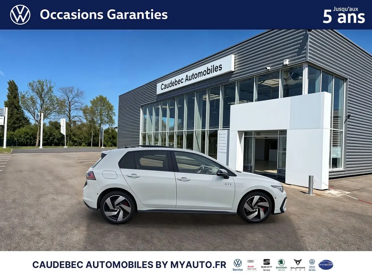 Vue latérale droite d'une Volkswagen Golf 1.5 eHybrid 272 DSG6 blanche, avec jantes alliage noires et logo GTE visible sur la porte avant.