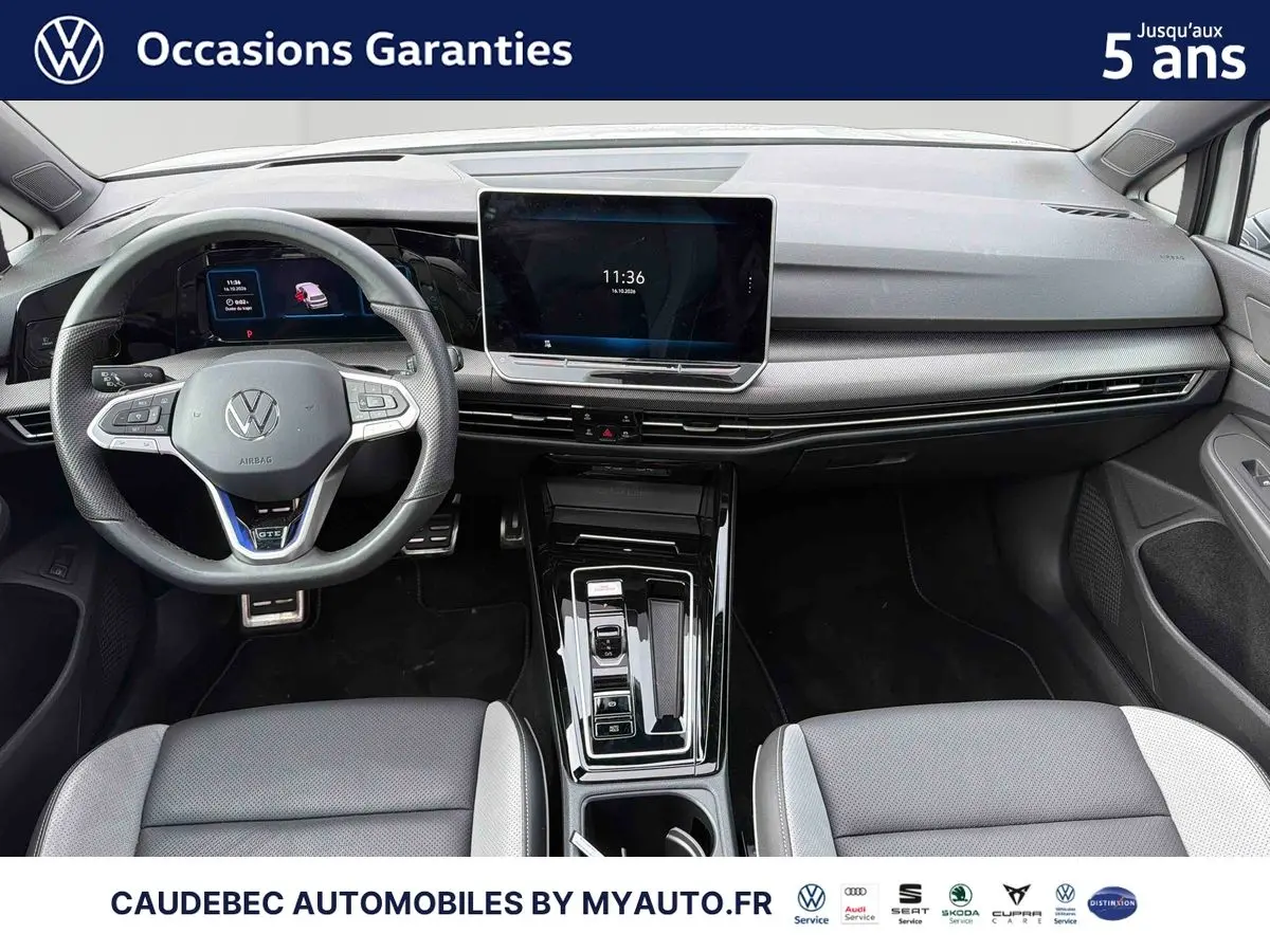 Vue intérieure avant de la Volkswagen Golf 1.5 eHybrid 272 DSG6 blanche, tableau de bord moderne avec écran tactile central et volant sport cuir.