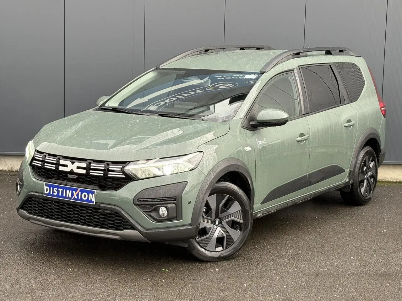 Dacia Jogger ECO-G 2025 en Kaki Lichen, vue 3/4 avant droit avec barres de toit et jantes spécifiques.