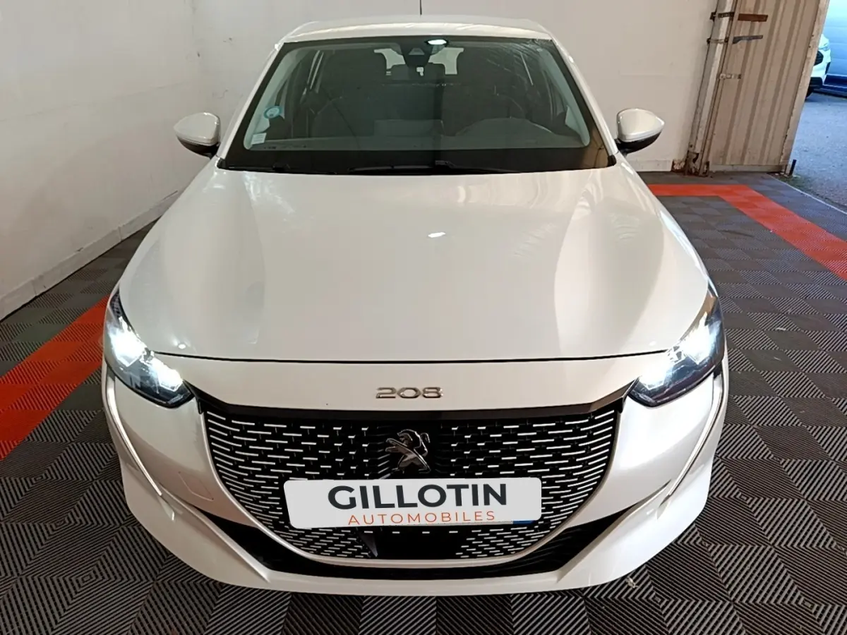 Vue avant d'une Peugeot 208 électrique Active Business blanche avec phares LED allumés en intérieur.