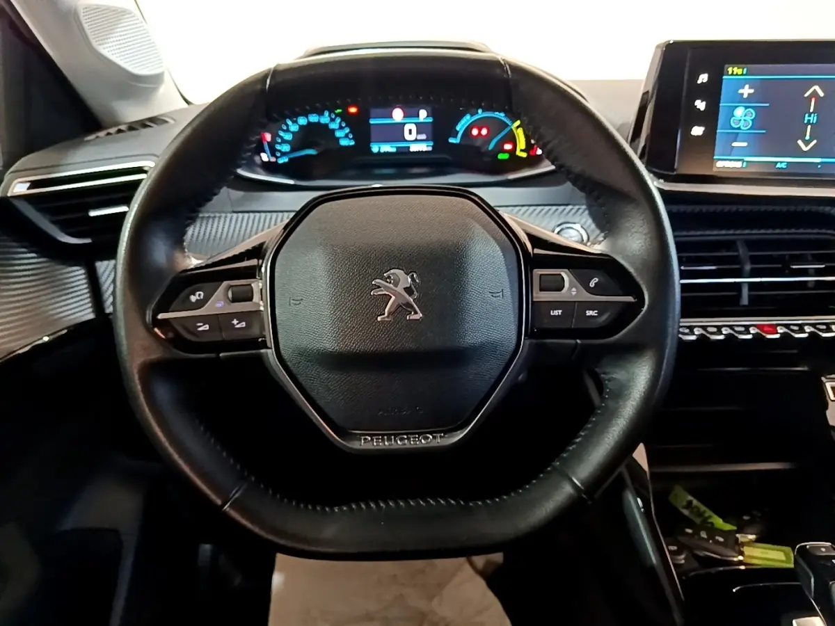 Vue intérieure centrée sur le volant cuir noir de la Peugeot 208 électrique avec tableau de bord digital et écran tactile.