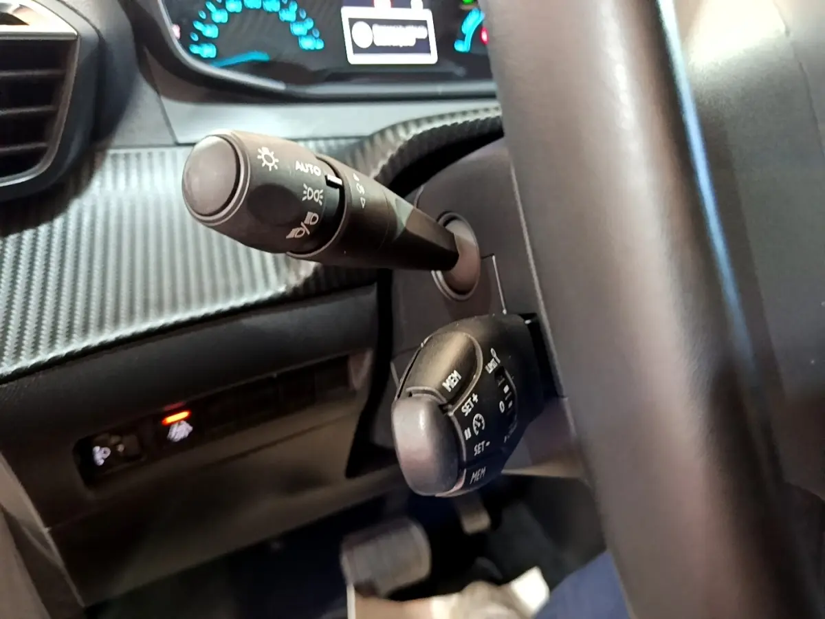 Gros plan sur la colonne de direction et commandes au volant d’une Peugeot 208 électrique blanche, version Active Business.