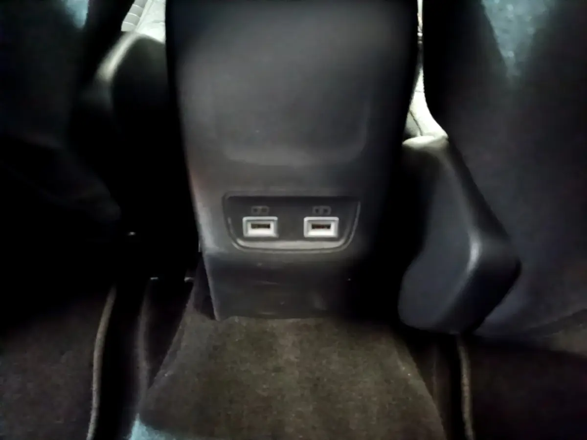 Vue rapprochée des ports USB arrière entre les sièges noirs d'une Peugeot 208 électrique blanche.