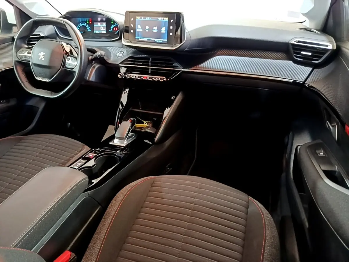 Intérieur de la Peugeot 208 électrique blanc, vue côté conducteur, tableau de bord moderne avec écran tactile central.