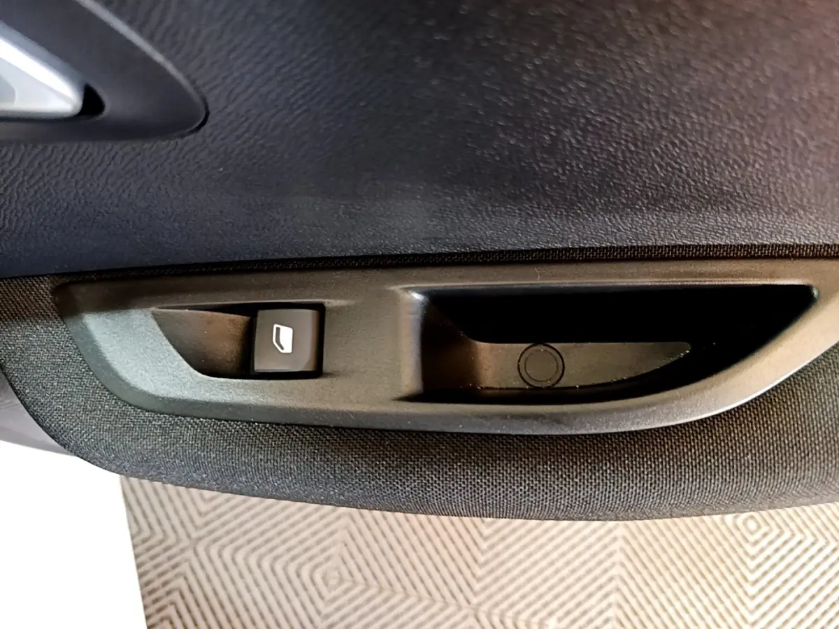Gros plan sur le bouton de commande de lève-vitre côté gauche intérieur d’une Peugeot 208 électrique blanche.
