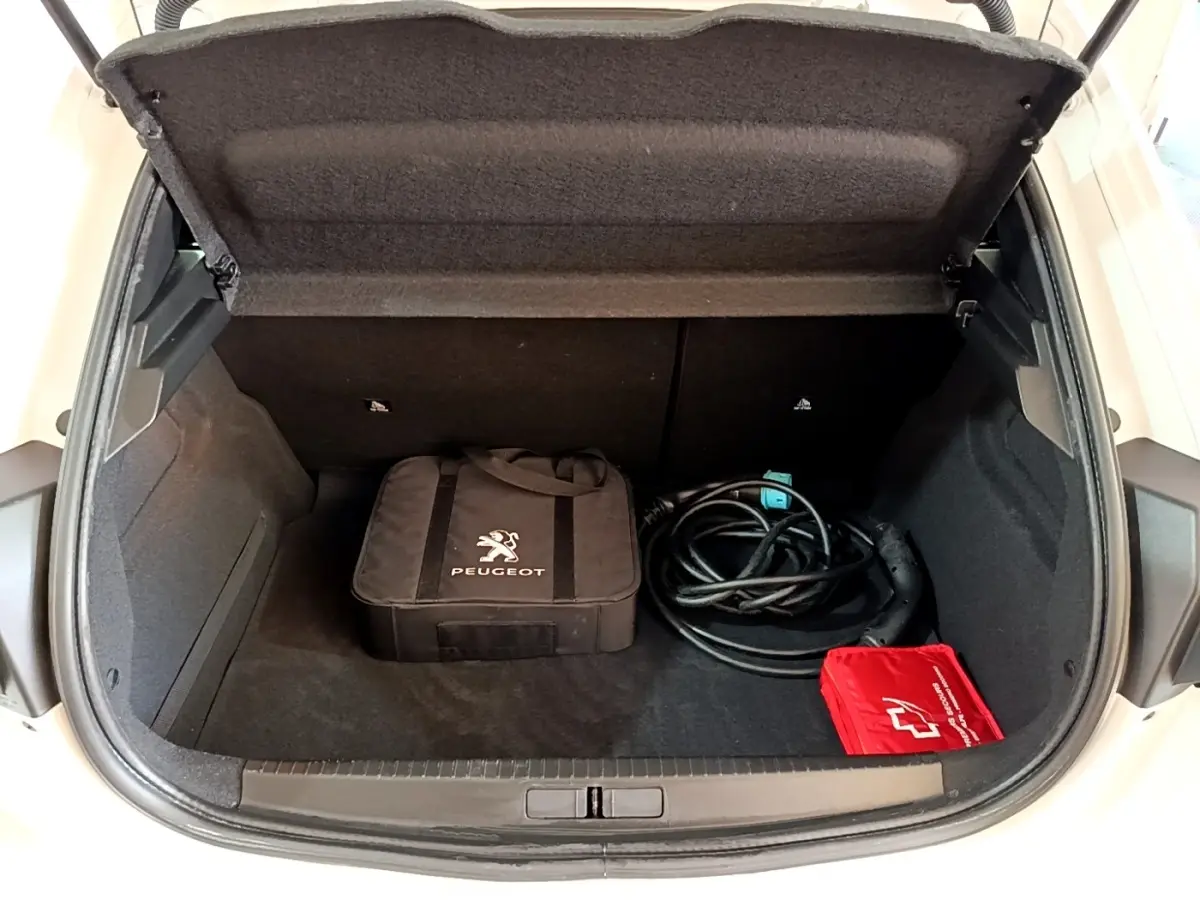 Vue plongeante sur le coffre ouvert blanc d'une Peugeot 208 électrique avec câble de recharge et sacoche Peugeot noire.