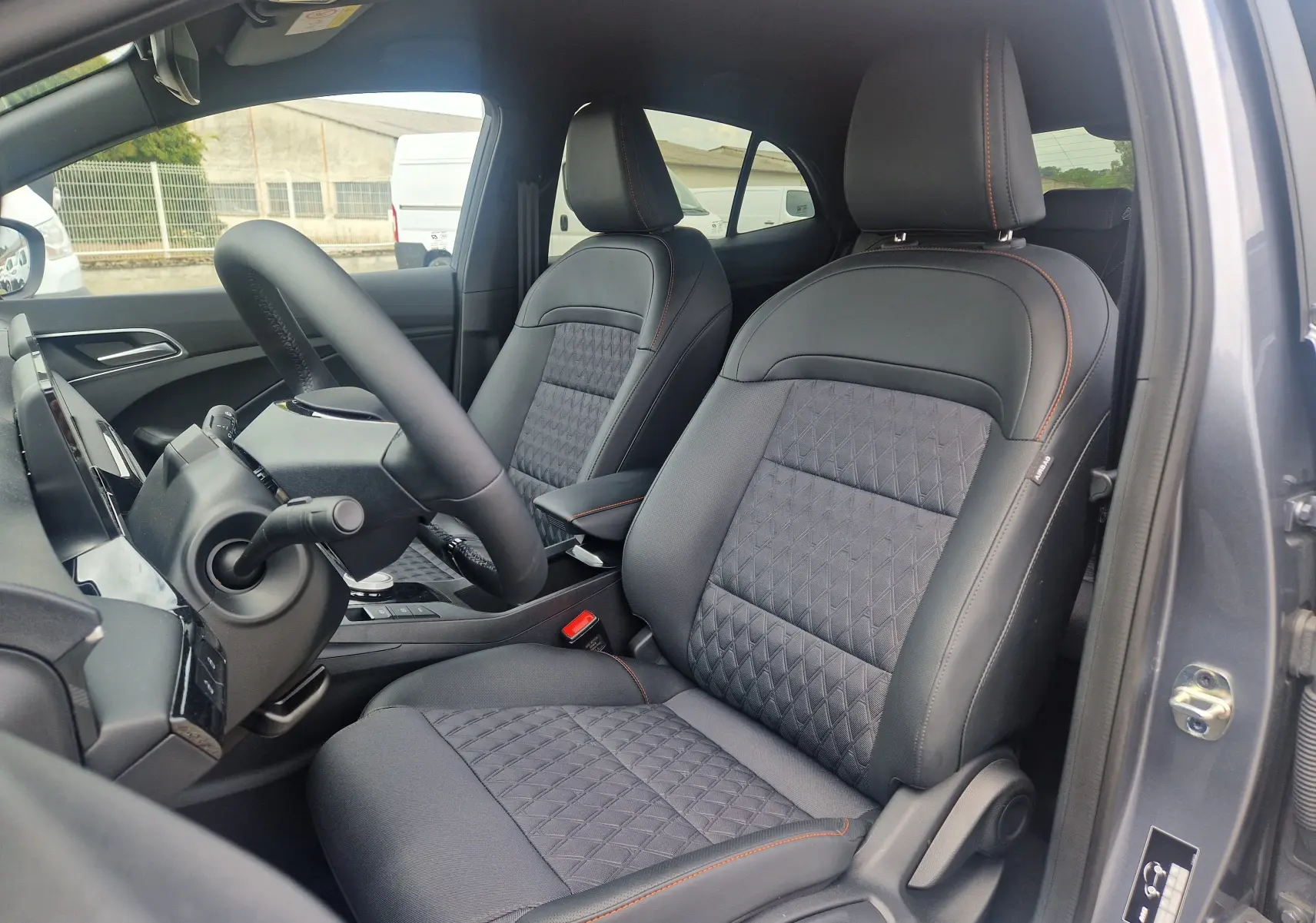 Vue intérieure côté conducteur du MG3 1.5L HYBRID+ 195CH Luxury 2026 en gris Hampstead, sièges tissu et cuir noir avec surpiqûres orange.