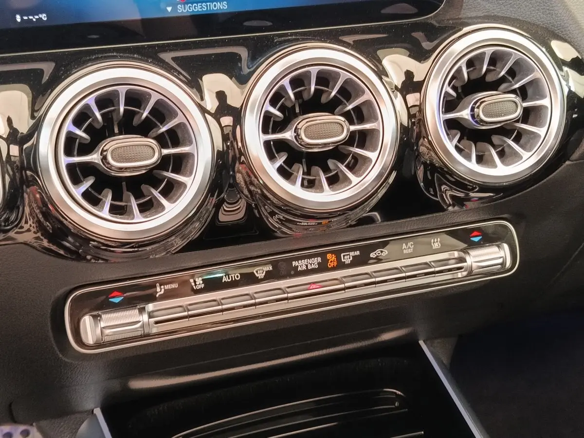 Détail intérieur du tableau de bord noir du Mercedes GLA 250 e AMG Line 2021, avec trois aérateurs ronds chromés et commandes climatisation.