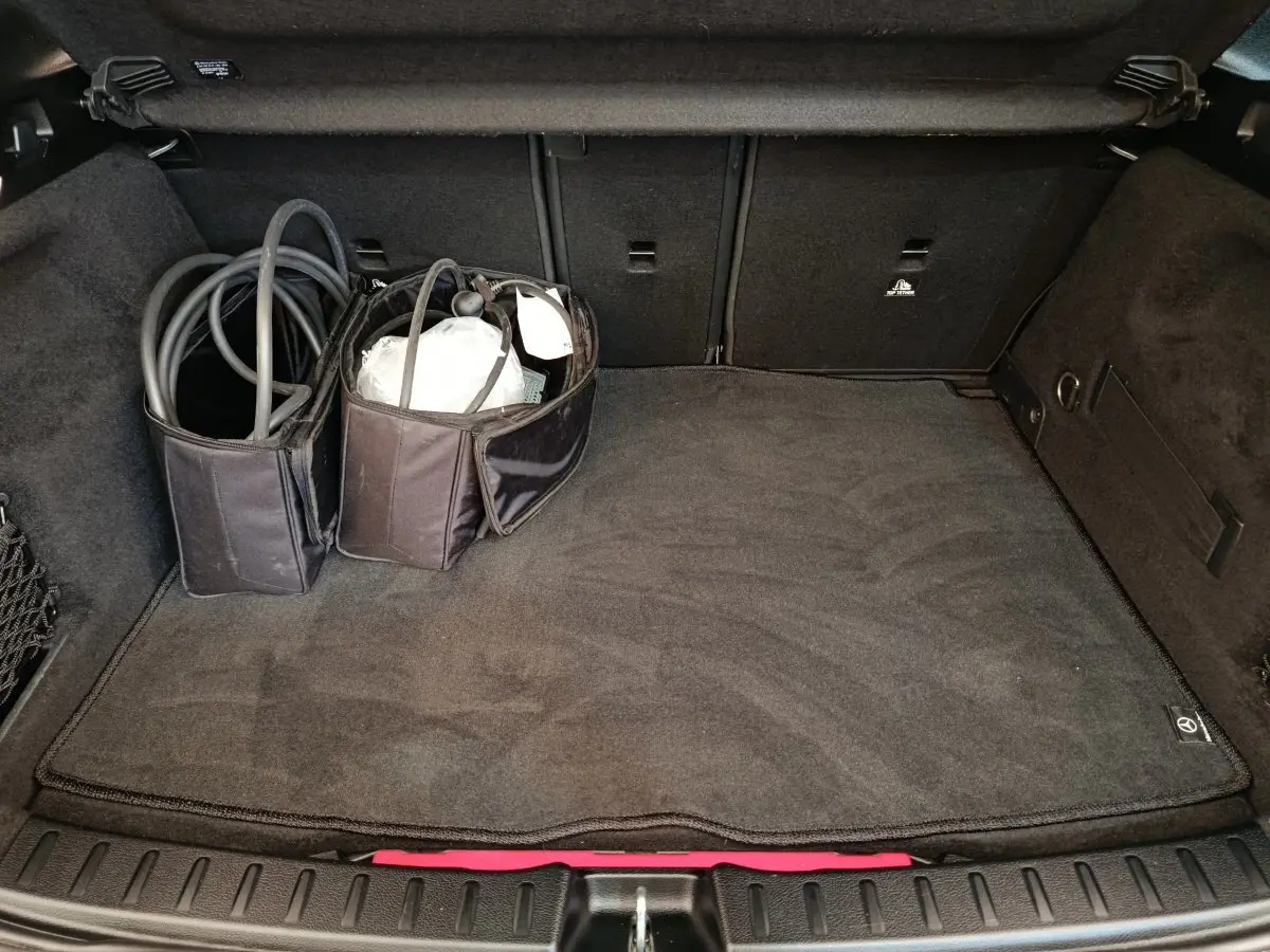 Coffre ouvert du Mercedes GLA 250 e AMG Line noir, vue plongeante montrant tapis et câbles de recharge rangés.