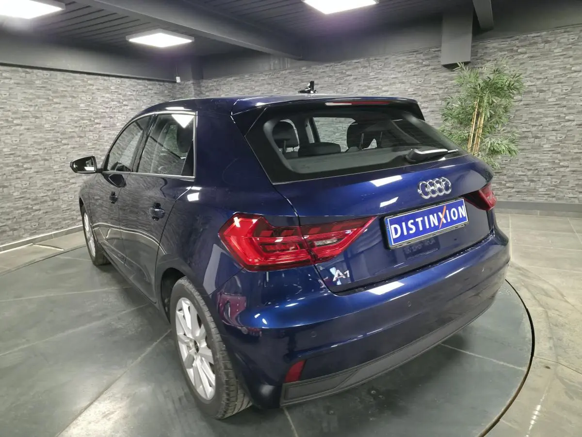 Audi A1 Sportback bleu métallisé vue 3/4 arrière droit avec feux LED et toit contrasté en intérieur showroom.