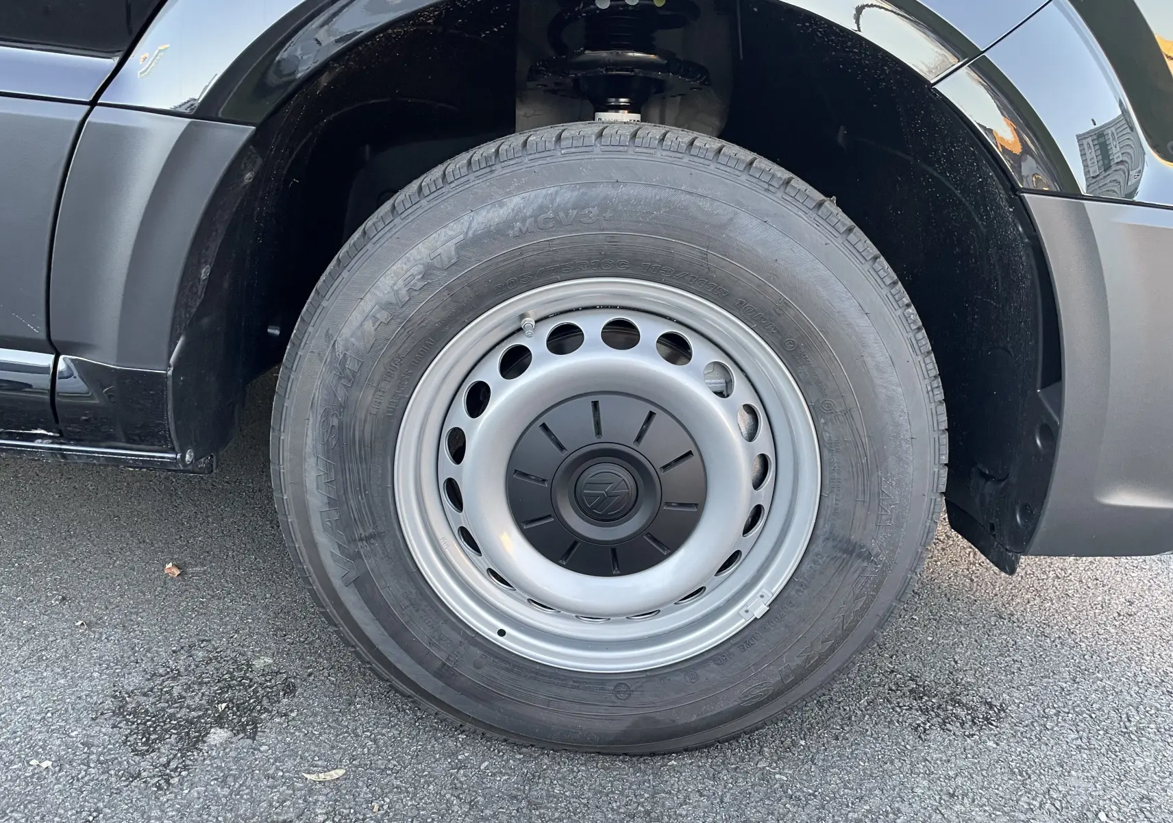 Gros plan sur la roue avant gauche du Volkswagen Crafter Van noir intense, mettant en valeur la jante acier et le logo VW central.