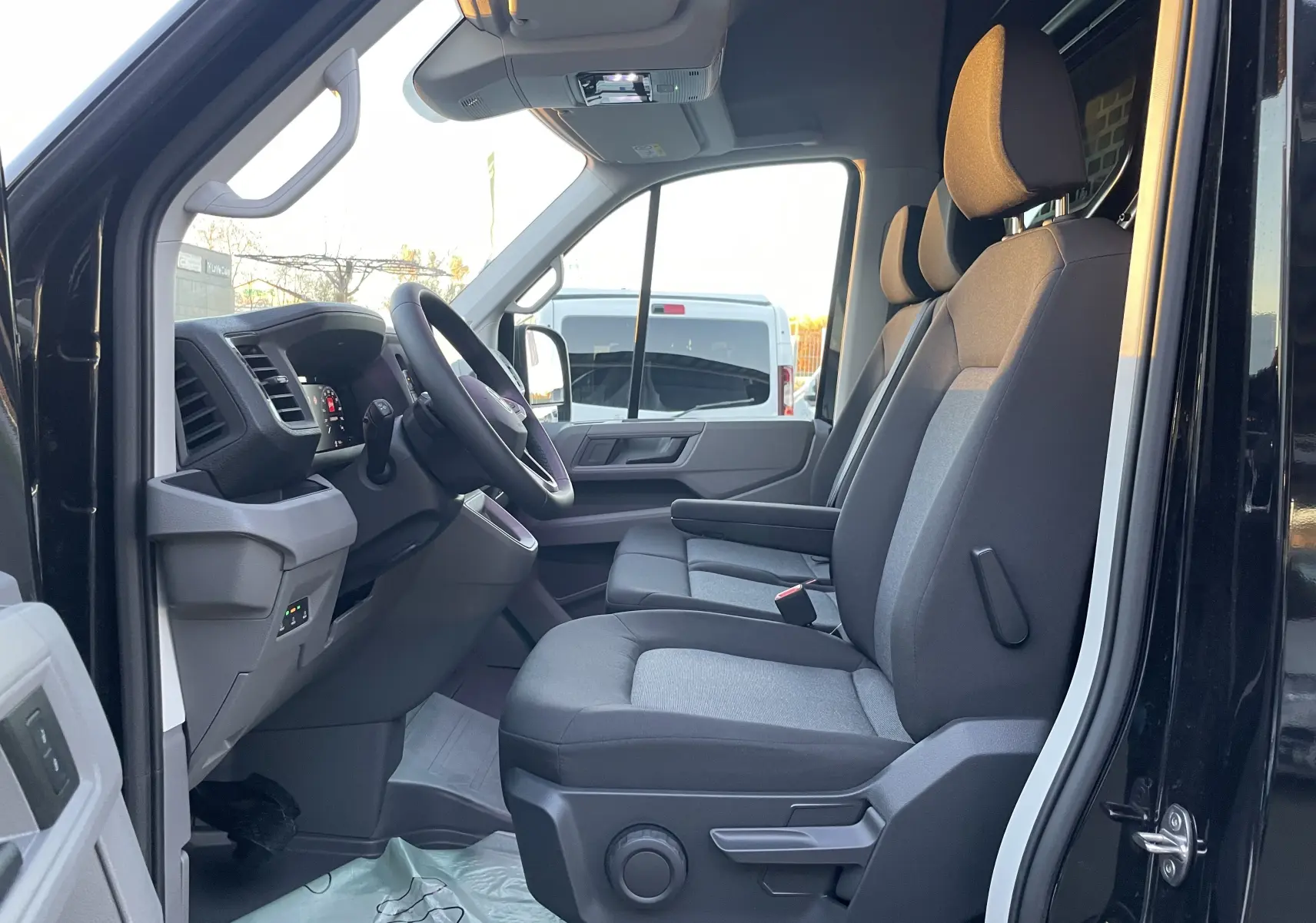Vue latérale intérieure côté conducteur du Volkswagen Crafter Van noir intense 2025, montrant les sièges avant et le tableau de bord.