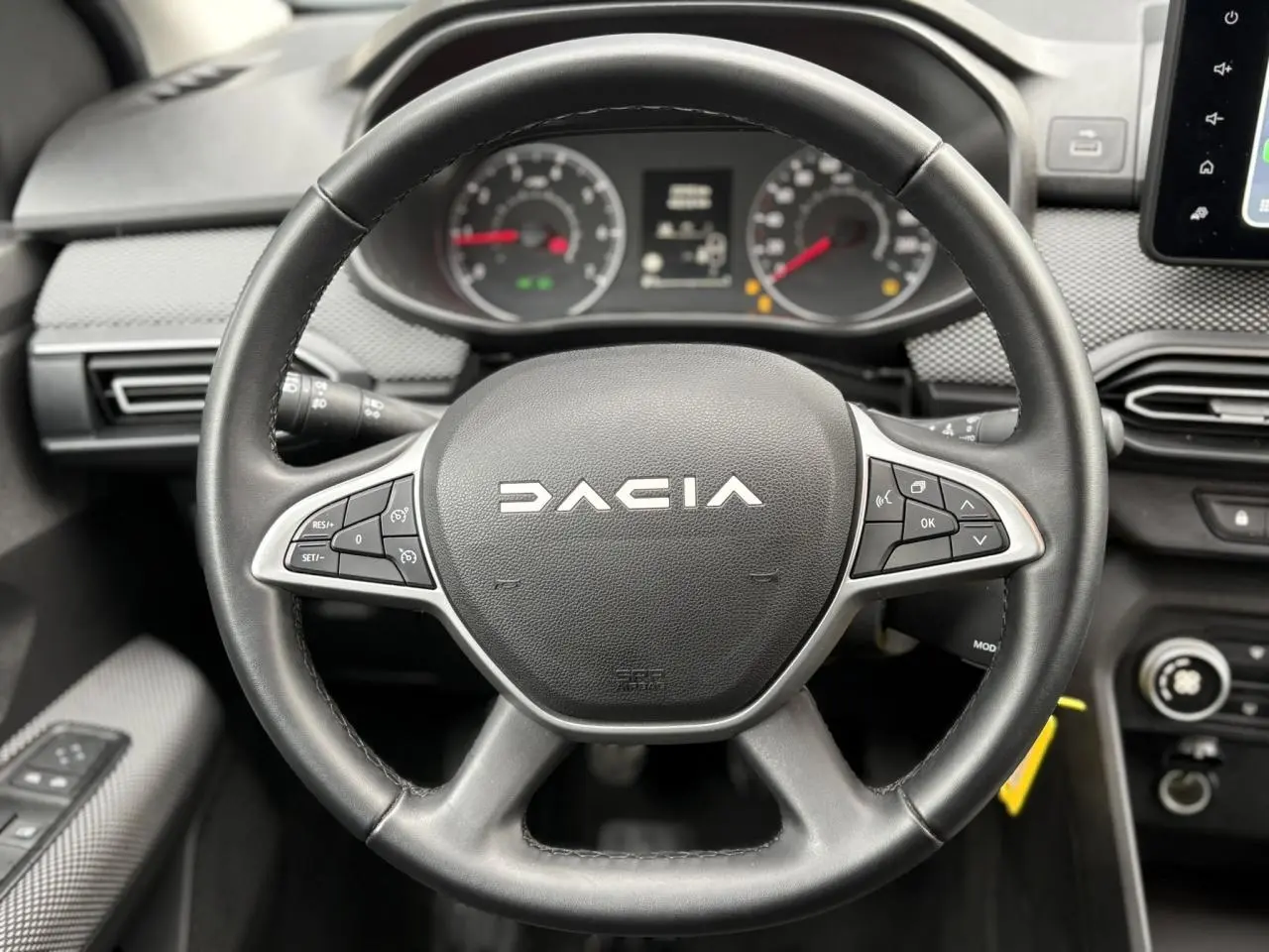 Vue rapprochée du volant noir DACIA JOGGER 2025 avec commandes intégrées et tableau de bord en arrière-plan.