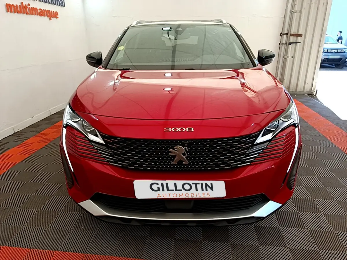 Vue frontale d'un Peugeot 3008 rouge avec calandre noire et logo lion central, dans un showroom intérieur.