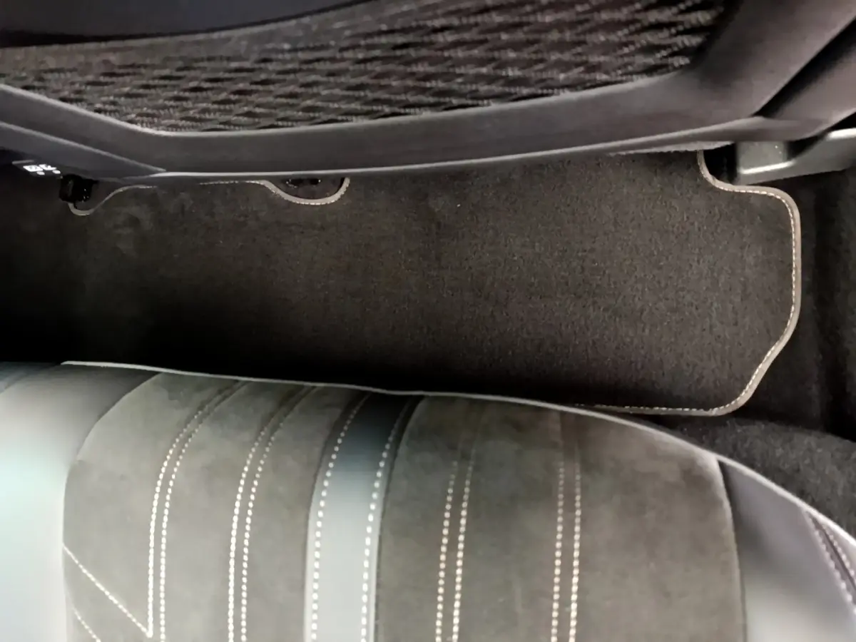 Vue rapprochée du tapis de sol noir et de la partie inférieure d’un siège en cuir et alcantara dans un Peugeot 3008 rouge.