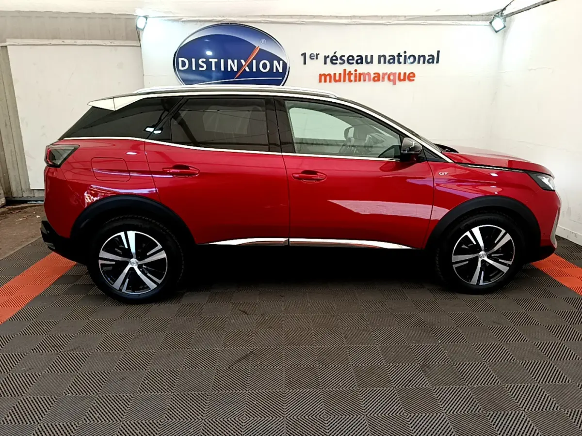 Vue de profil côté gauche d’un Peugeot 3008 GT rouge avec jantes alliage et toit noir dans un showroom.