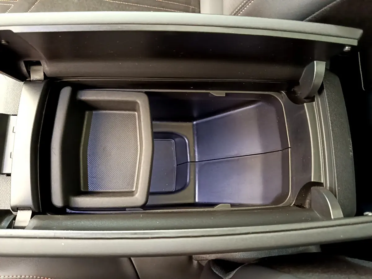 Vue plongeante sur le rangement central noir ouvert du Peugeot 3008 GT rouge, intérieur sobre et fonctionnel.