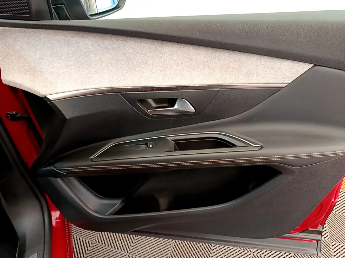 Vue intérieure côté gauche de la porte rouge d’un Peugeot 3008 GT avec garniture noire et surpiqûres contrastantes.