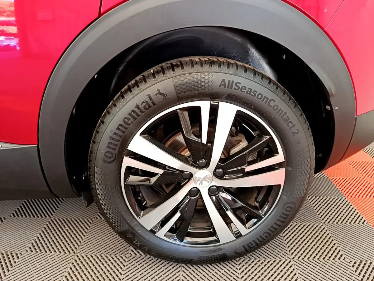 Gros plan sur la roue avant droite d’un Peugeot 3008 rouge, mettant en valeur la jante alliage bicolore et le pneu Continental.