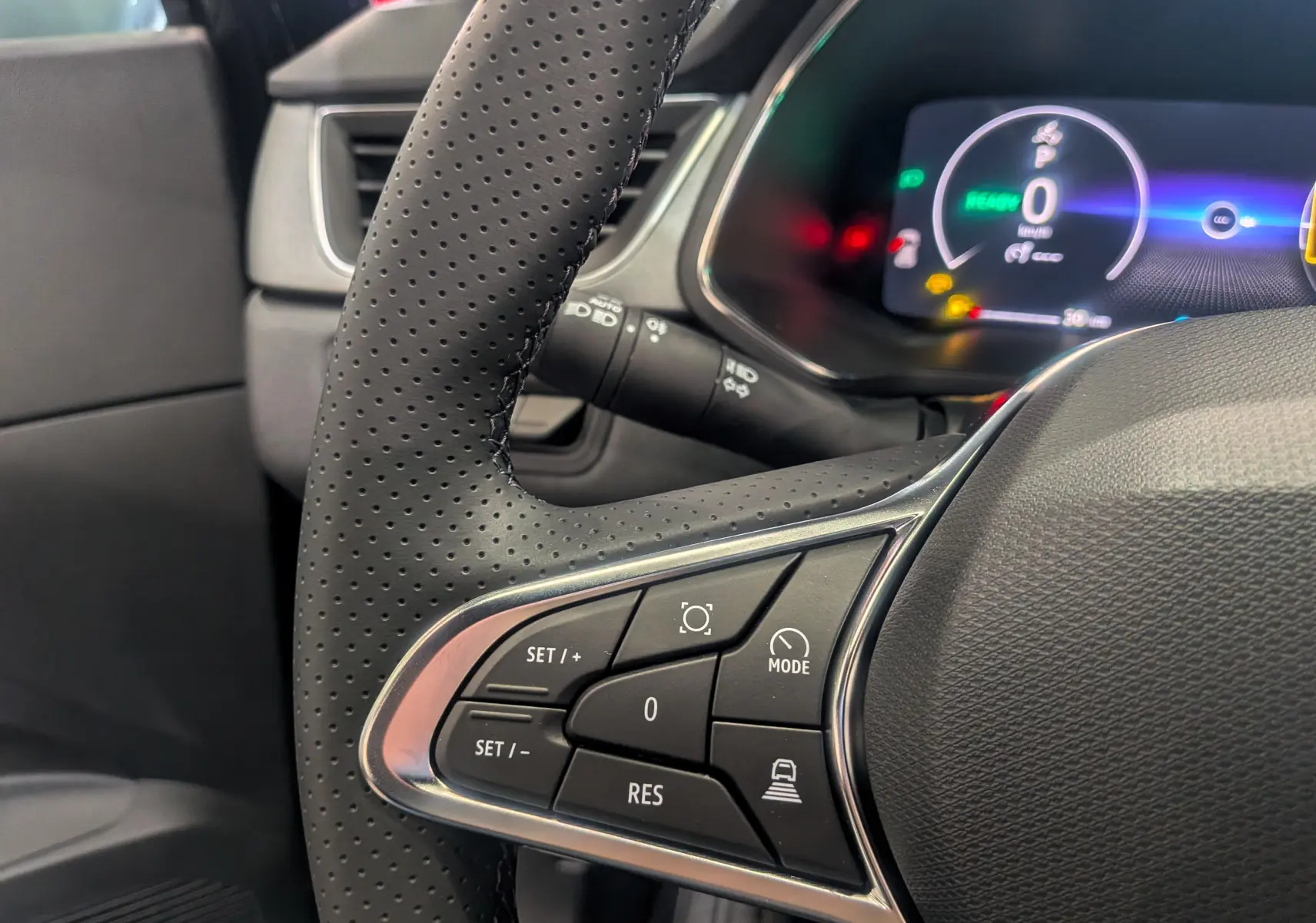 Gros plan sur le volant perforé et les commandes multifonctions du Renault Captur E-Tech 2026, tableau de bord numérique en arrière-plan.