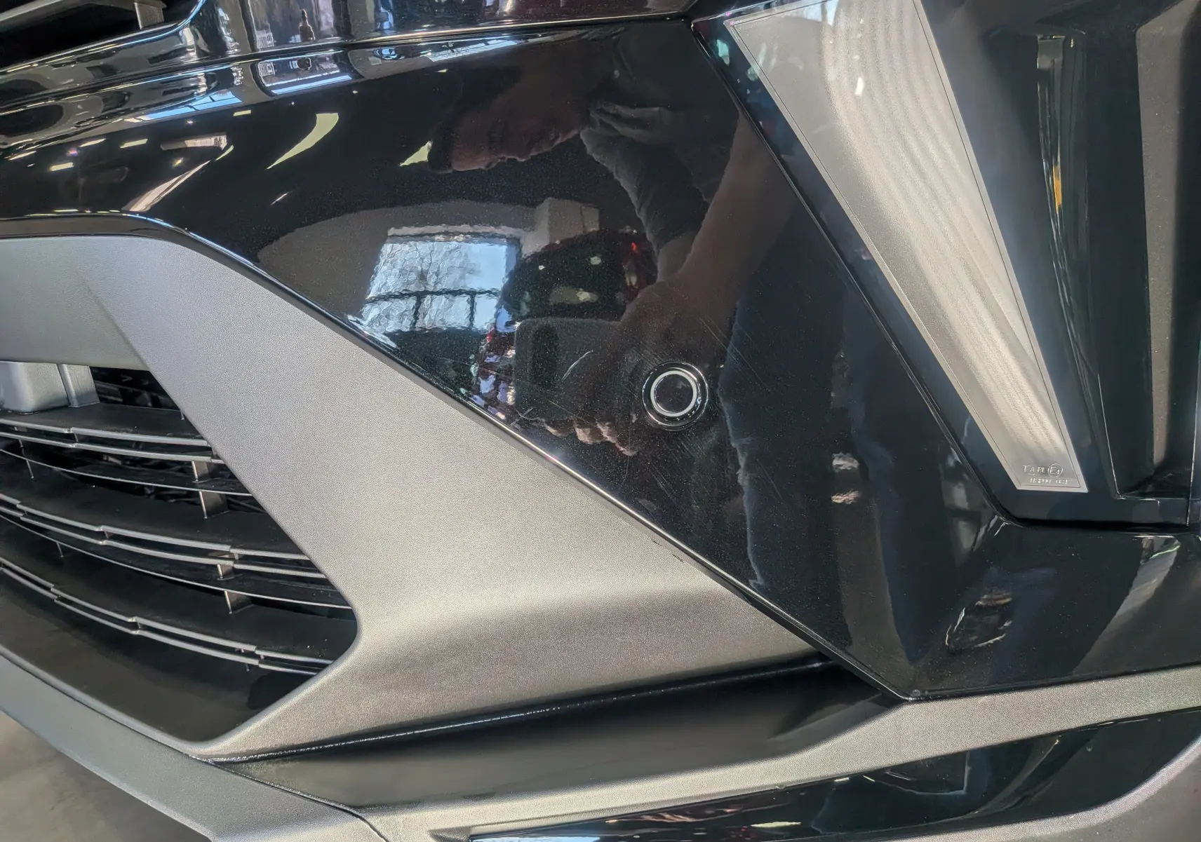 Gros plan sur le pare-chocs avant noir du Renault Captur E-TECH avec capteur de stationnement circulaire visible.